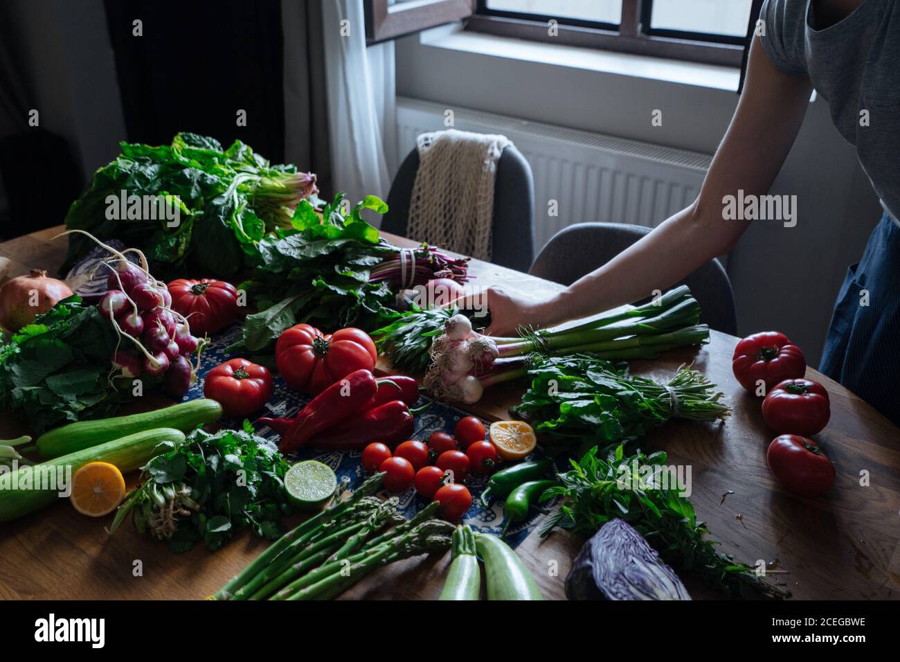 Crop view of female hands taking potherbs from elegant table with fresh healthy vegetable and fruit cooking ingredients from above Stock Photo