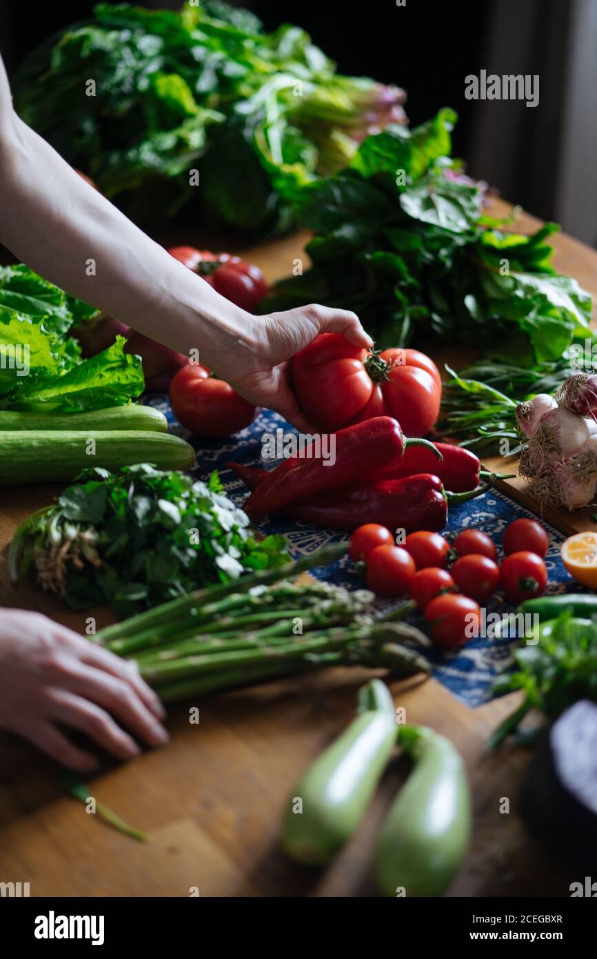 Crop view of female hands taking potherbs from elegant table with fresh healthy vegetable and fruit cooking ingredients from above Stock Photo