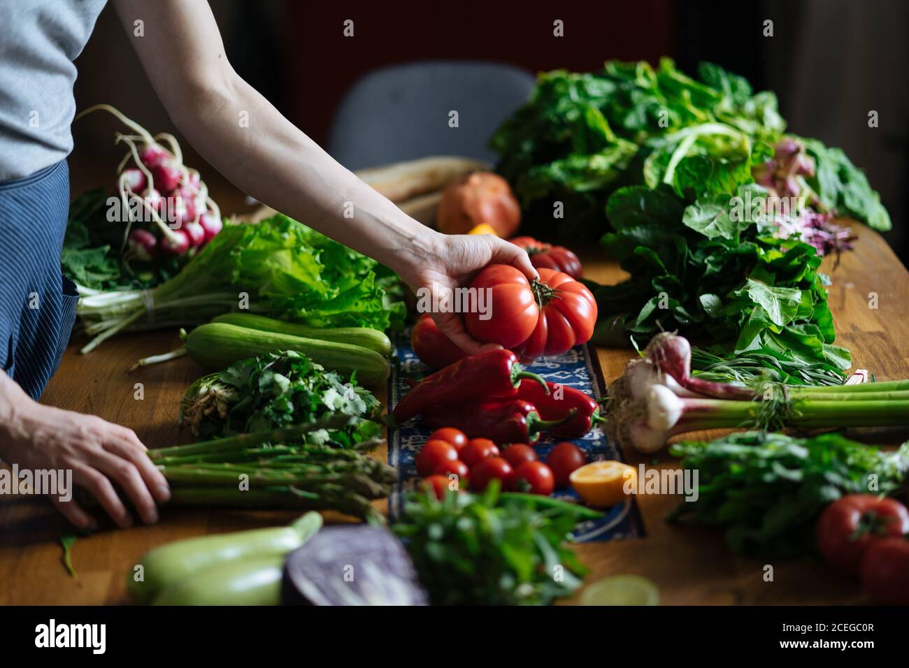 Crop view of female hands taking potherbs from elegant table with fresh healthy vegetable and fruit cooking ingredients from above Stock Photo