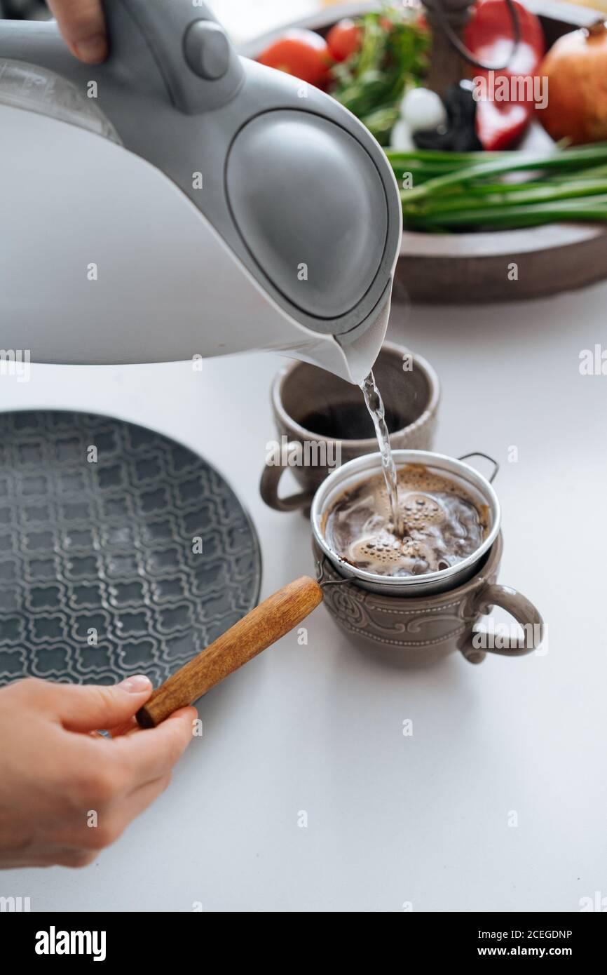 https://c8.alamy.com/comp/2CEGDNP/crop-hands-pouring-hot-water-from-kettle-into-beautiful-ceramic-mug-with-small-filter-scoop-in-it-standing-on-table-with-cooking-ingredients-2CEGDNP.jpg