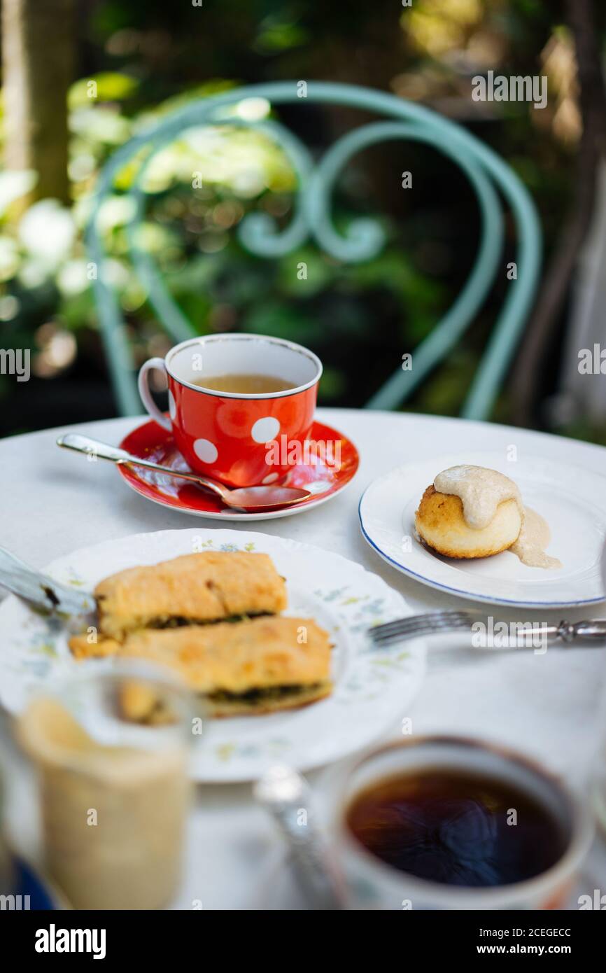 Red ceramic polka-dotted mug on saucer with spoon?and light drink in it standing on white round table with elegant jars with lace ribbons outdoors from above Stock Photo