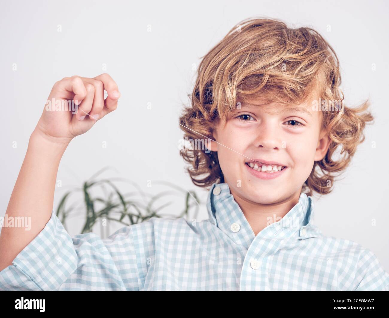 boy in shirt pulling tooth out with thread while looking at camera