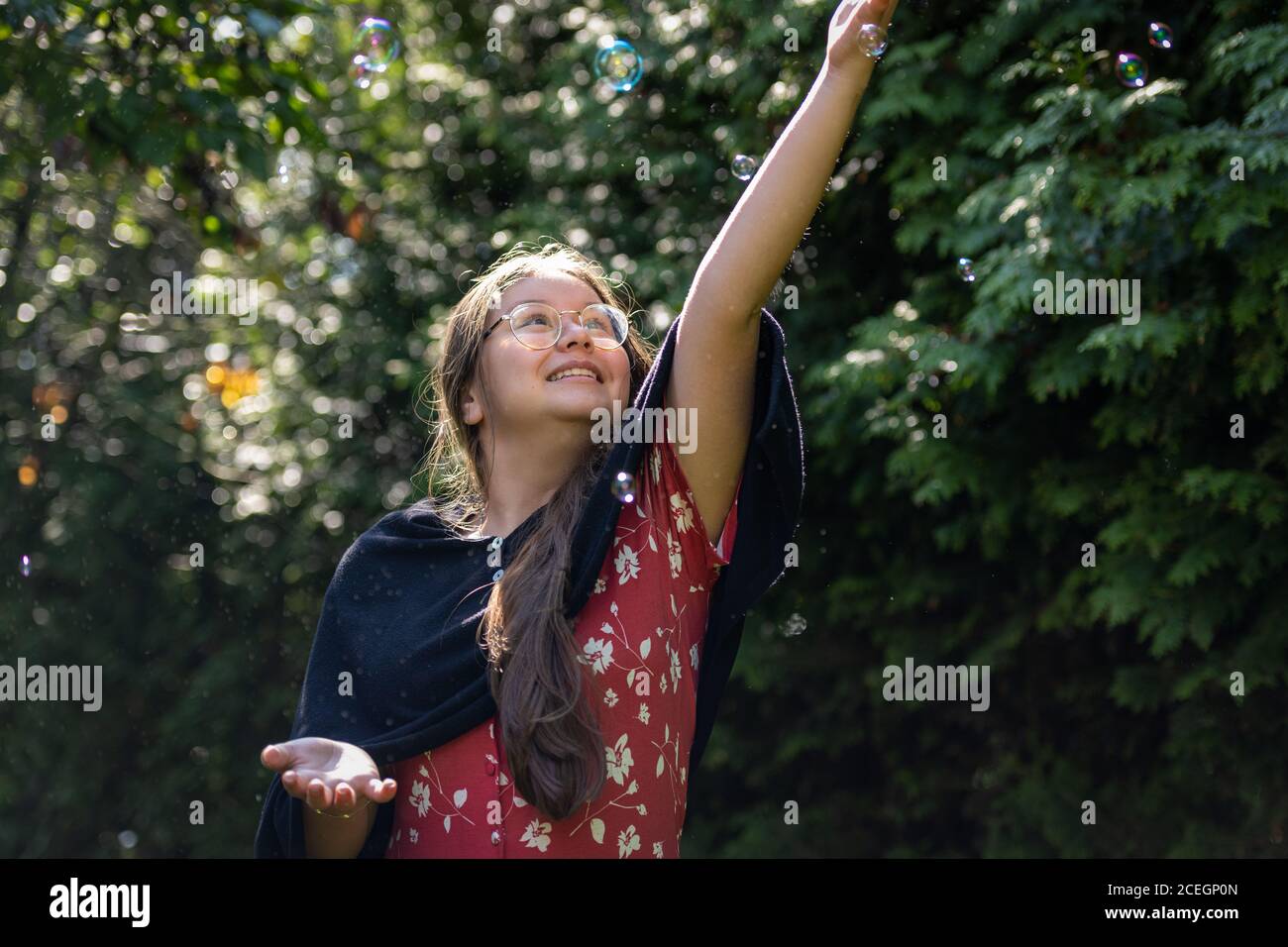 A preteen girl chasing soap bubbles. Shallow depth of field. Green leaves background. Stock Photo