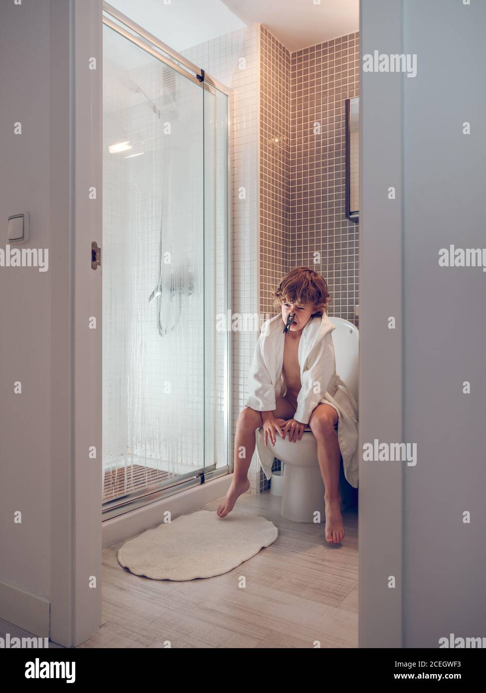 boy in bathrobe sitting on toilet with newspaper Stock Photo