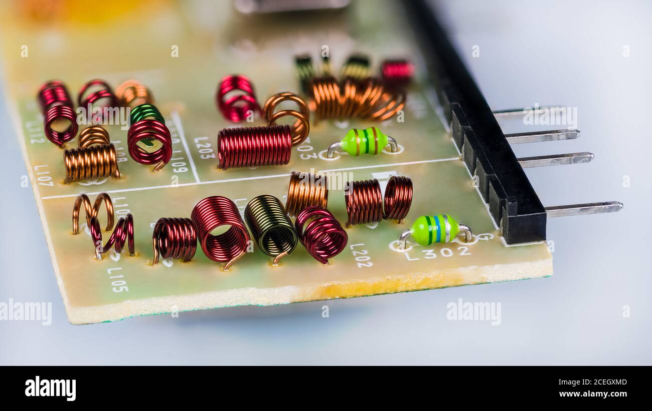 Red radio frequency inductors or green chokes inside RF module of television receiver.Copper wire winding with air core. Electronic induction coils. Stock Photo