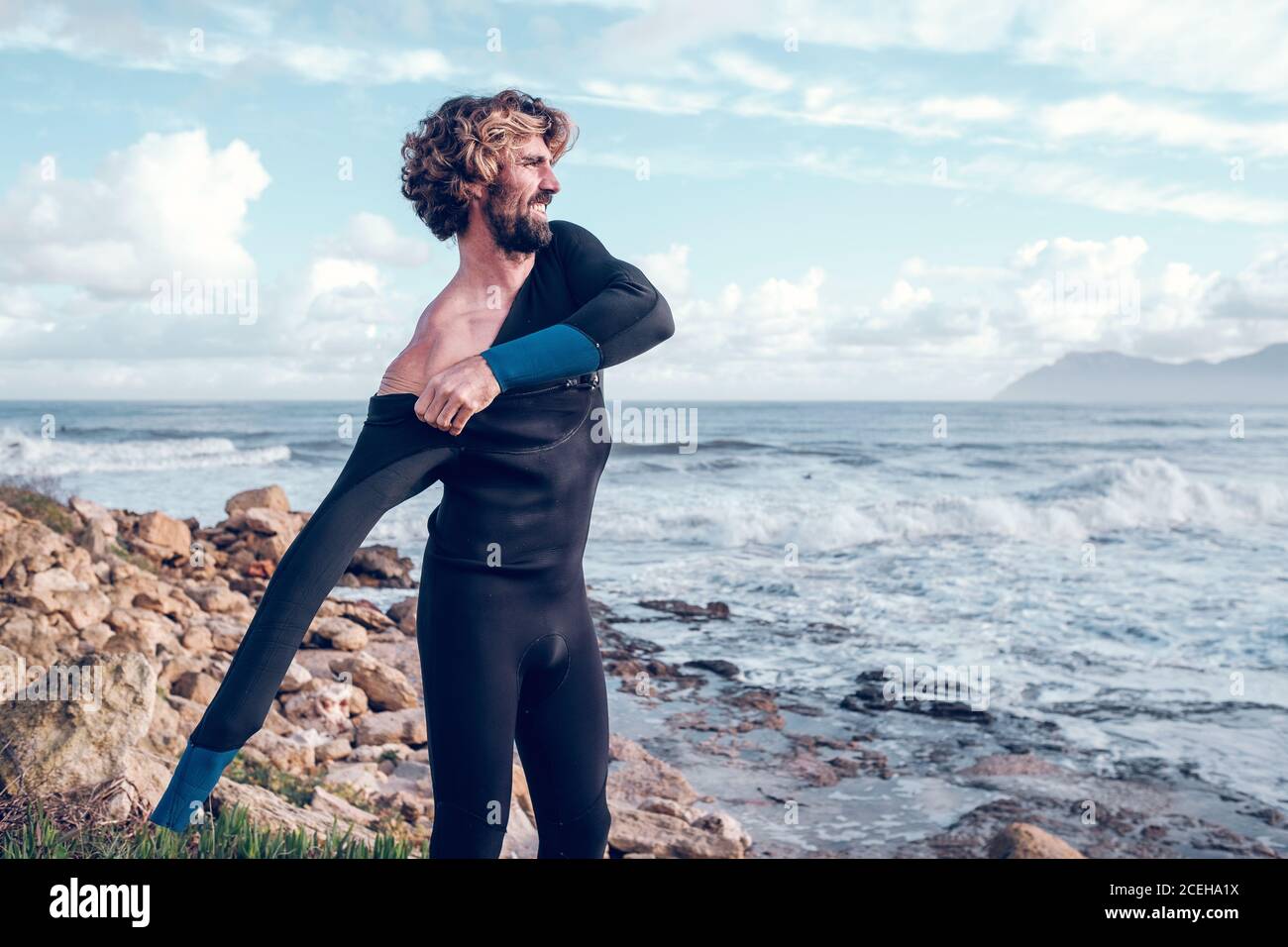 Young man putting on wetsuit near sea Stock Photo Alamy