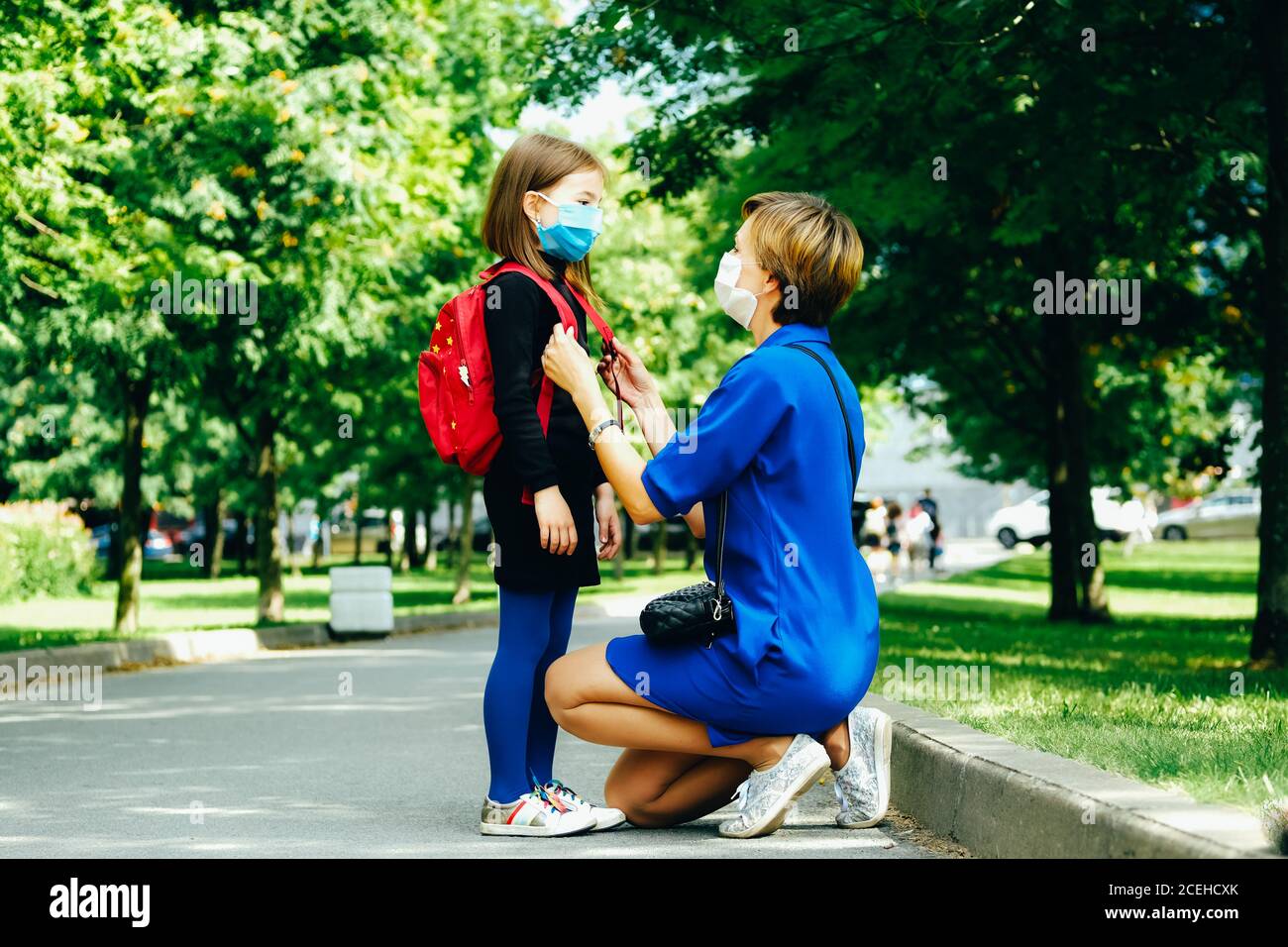 mother wearing a protective mask is seeing off her daughter. Back to school concept. Stock Photo