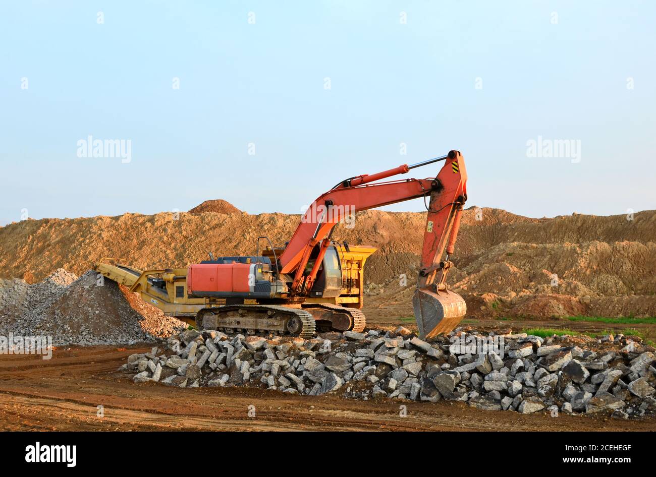 Heavy tracked excavator load stone, old asphalt or concrete waste into a mobile jaw crusher machine. Crushing and processing into gravel for recycling Stock Photo