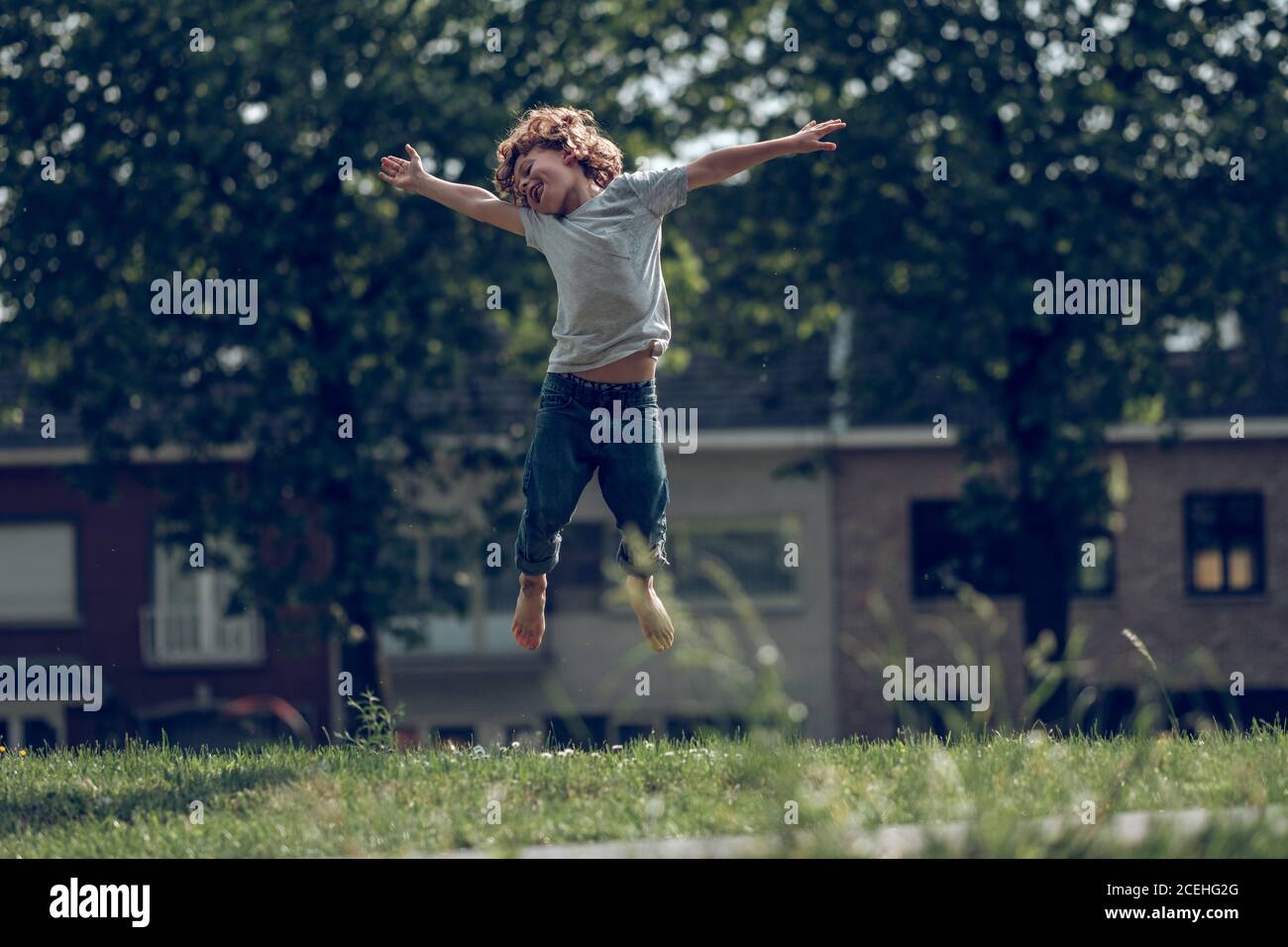 Cheerful kid in denim and t-shirt jumping high above grass having fun and looking super happy Stock Photo