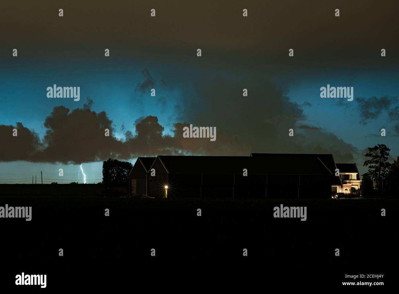 Night scene where a lightning bolt strikes down to earth behind a farm