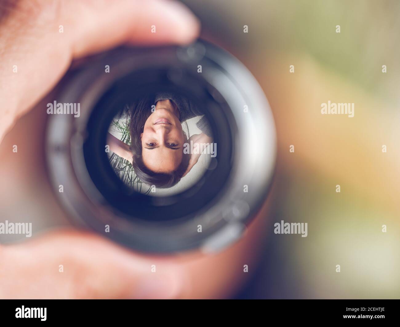 Closeup shot of crop hand holding lens with reversed image of smiling Woman on blurred background Stock Photo