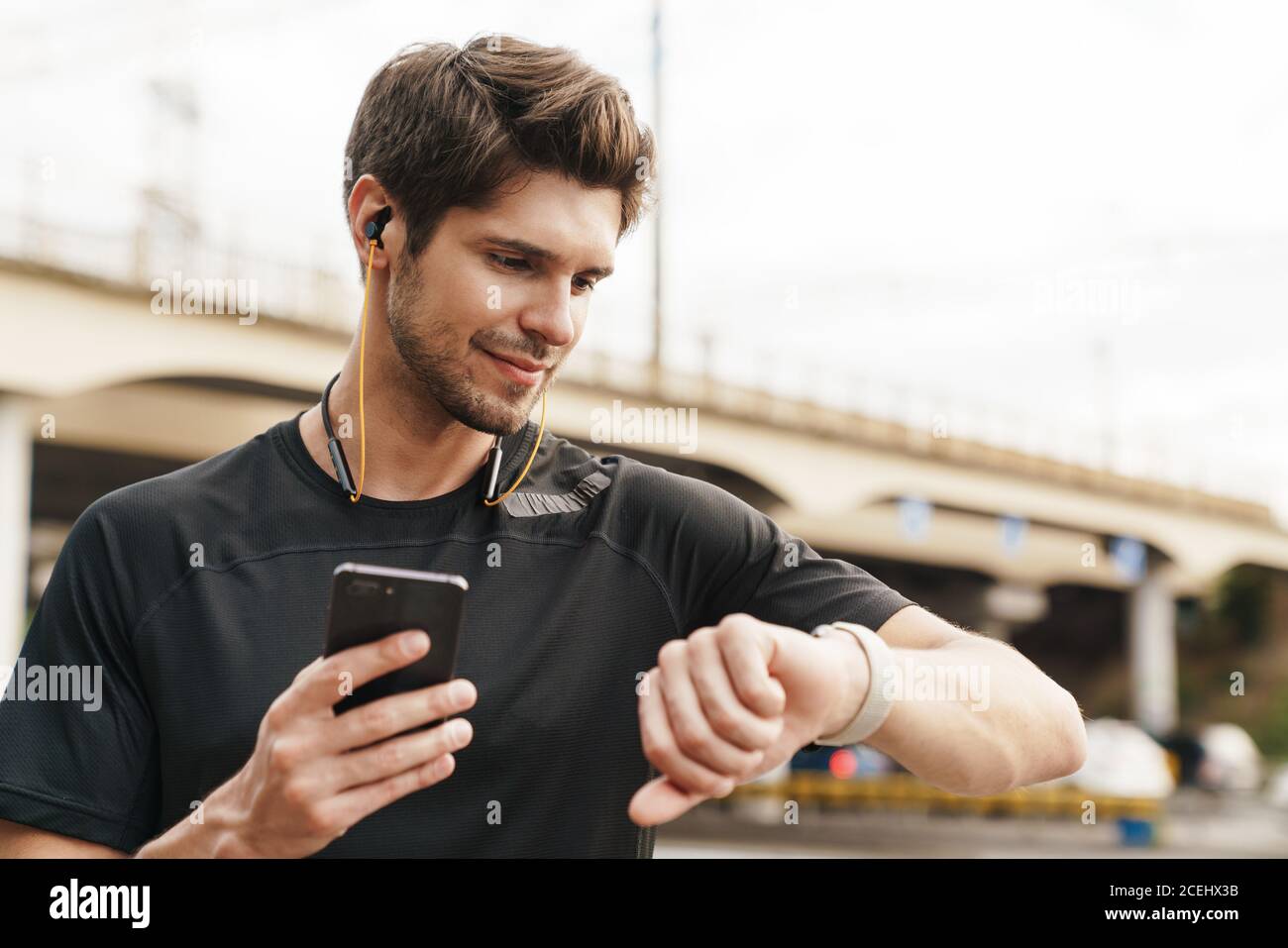 Image of pleased sportsman in earphones using cellphone and smartwatch