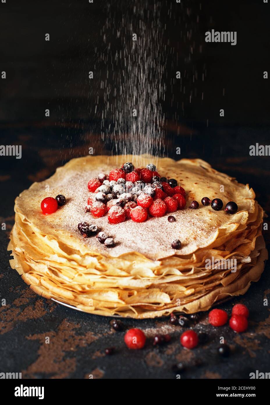 Russian pancakes with berries sprinkled with sugar powder in front of dark background. Pancake week - The ancient Slavic festival of seeing off the wi Stock Photo
