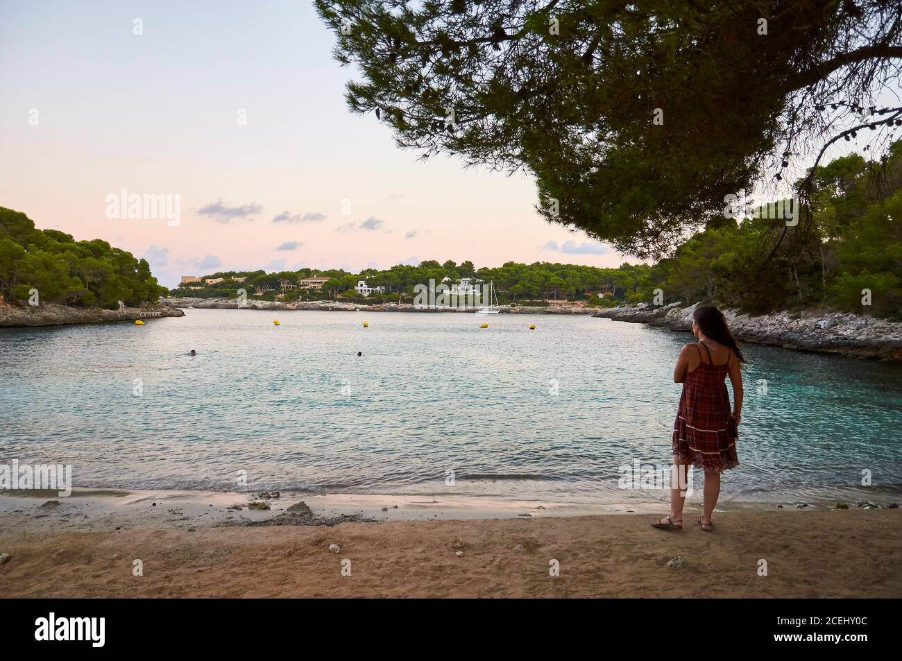 Woman at Caló des Homes Morts beach shore at sunset with villas in the background (Santanyí, Majorca, Balearic Islands, Mediterranean sea, Spain) Stock Photo