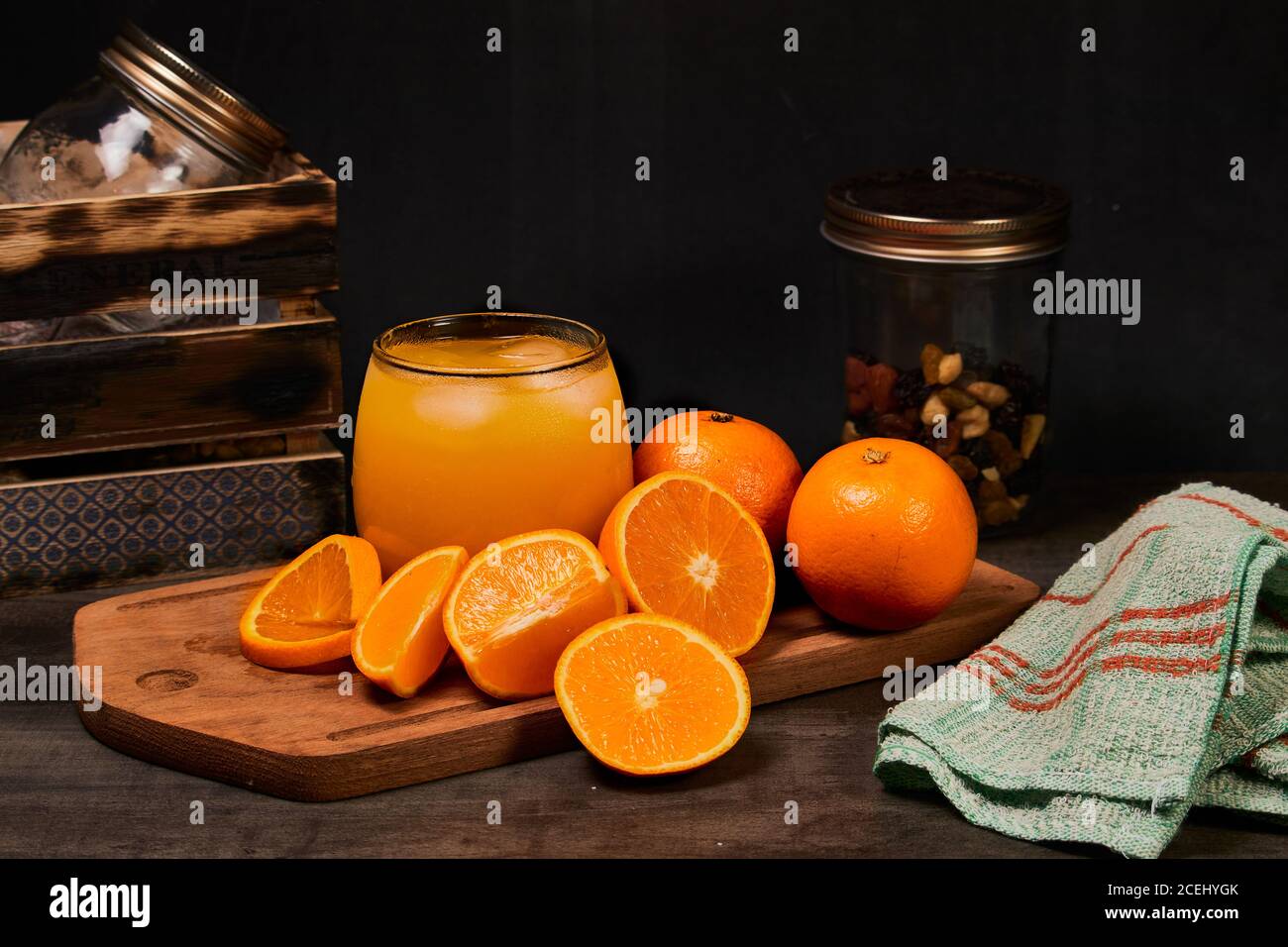 refreshing glass with fresh orange juice, ice and oranges on a wooden table in dark background Stock Photo