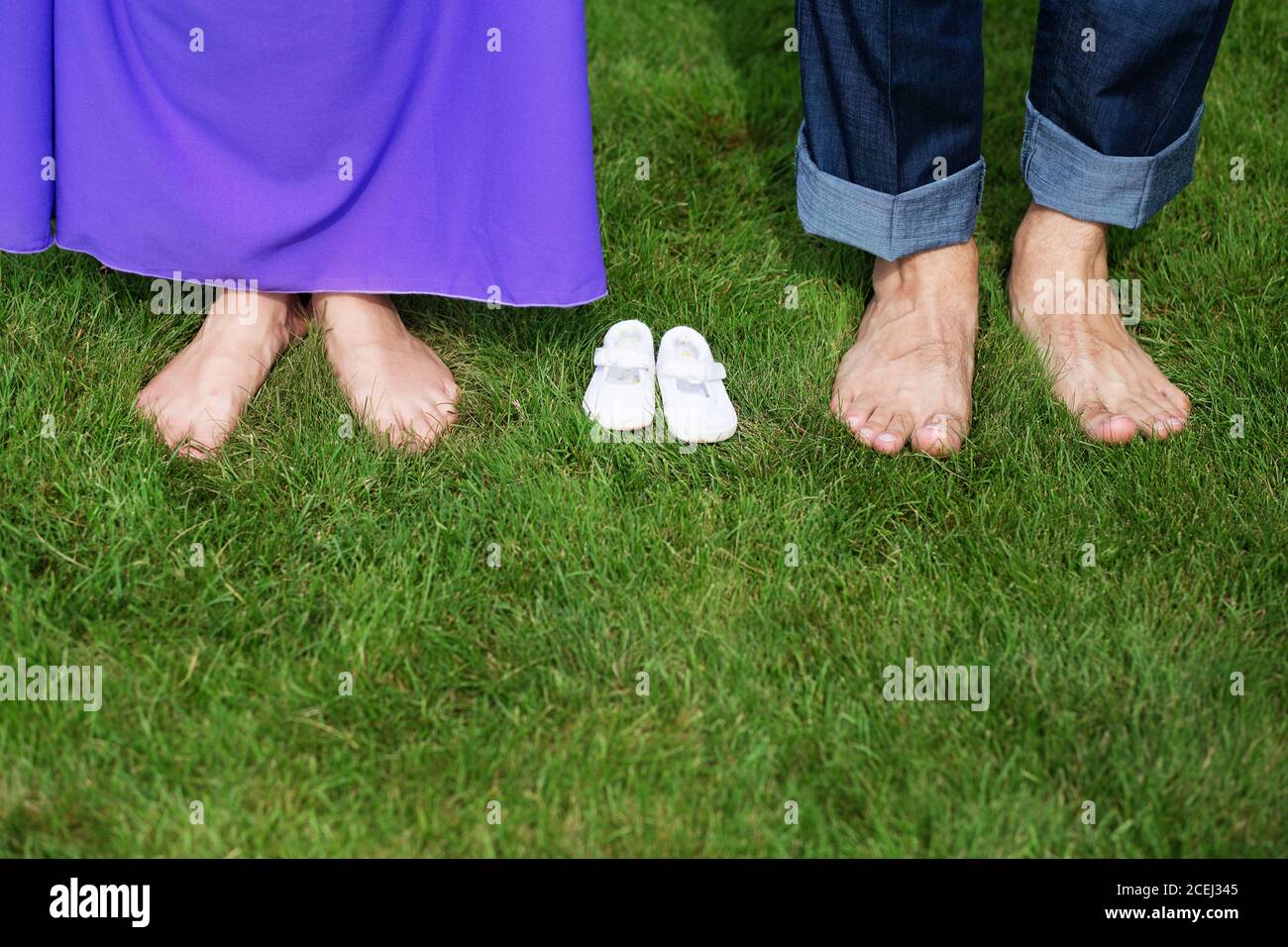Young Pregnant Couple Feet barefoot on green grass With Newborn Baby