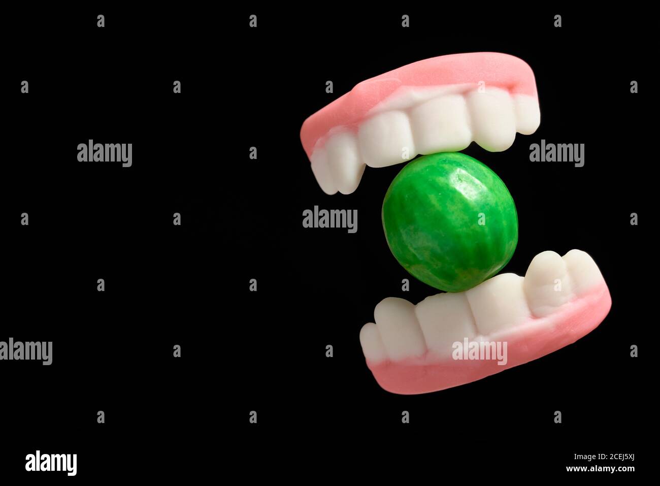 Halloween treats, gummy teeth biting a watermelon gum, on black