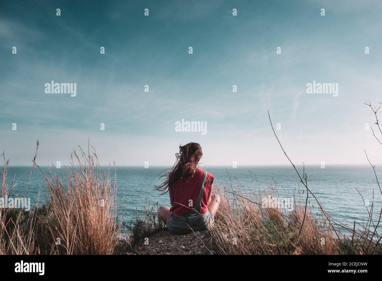 Back view of tourist Woman sitting on stone and looking at seascape ...