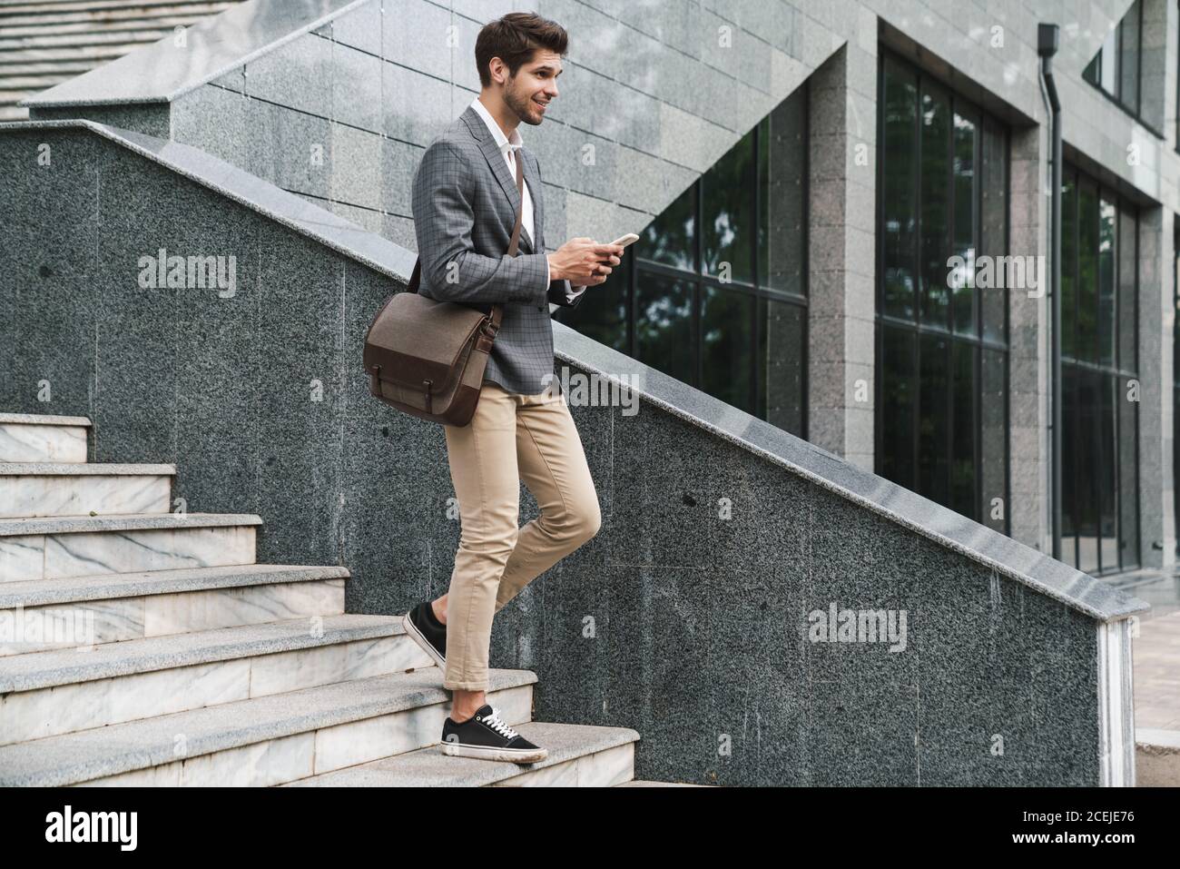 Image of cheerful handsome business man outdoors using mobile phone while going down the stairs Stock Photo