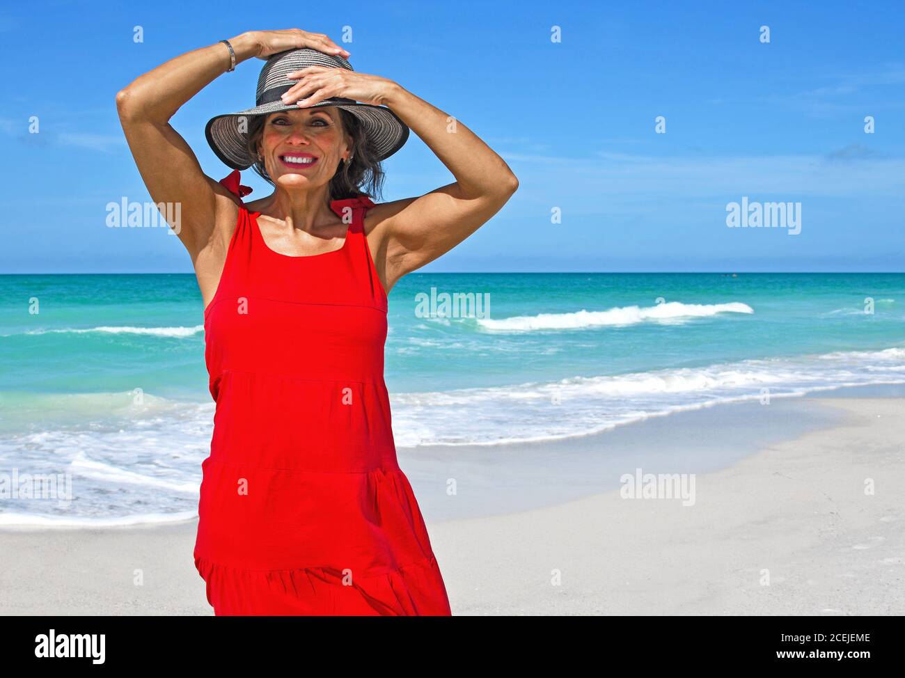 Beautiful Mature Woman Wearing a Red Summer Dress on the Beach Stock Photo