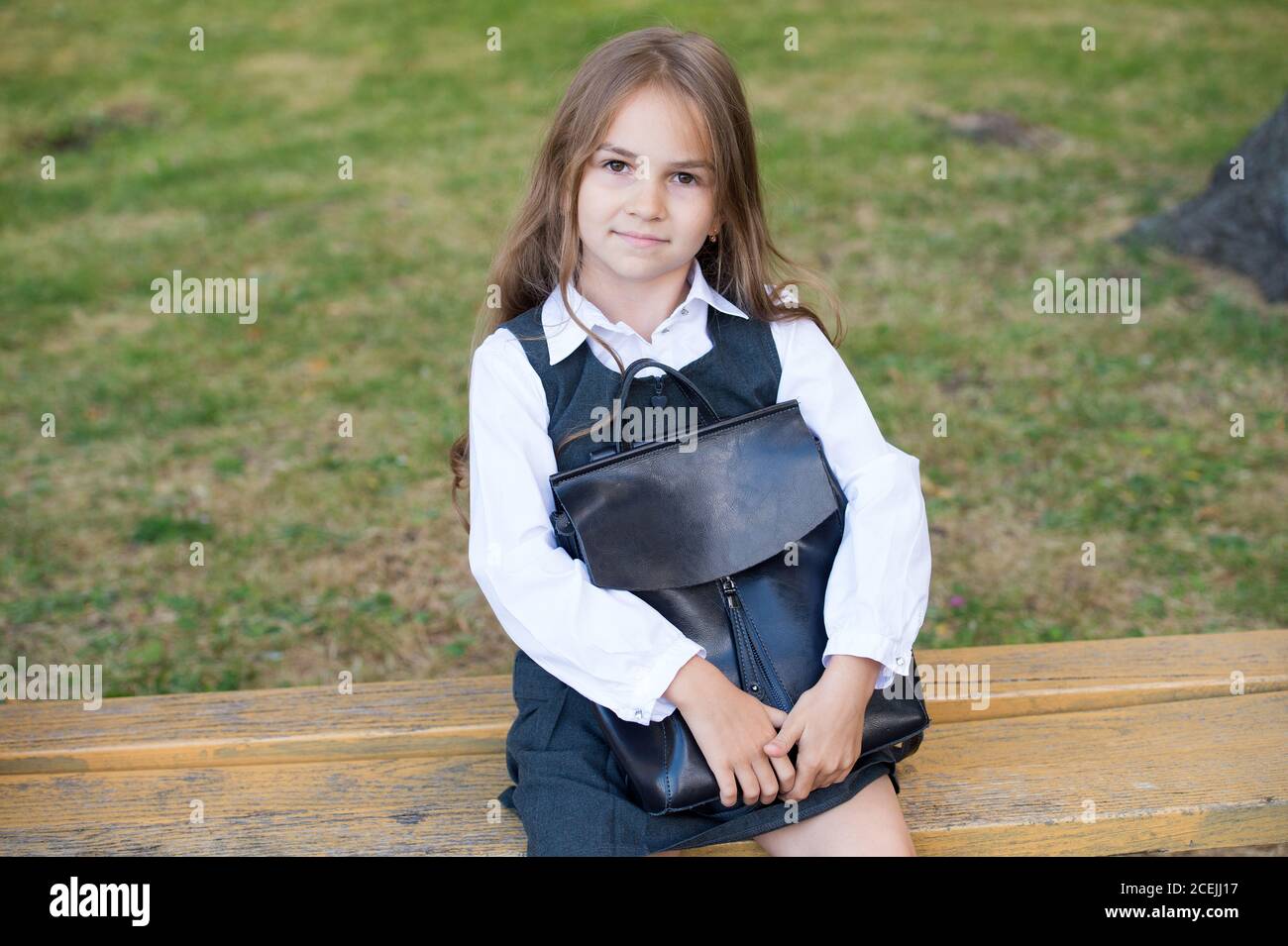 Bright from start. Little kid with school bag sit on bench. Formal schooling. Back to school supplies. September 1. Home schooling. Private teaching. Knowledge day. Encouraging developmental growth. Stock Photo