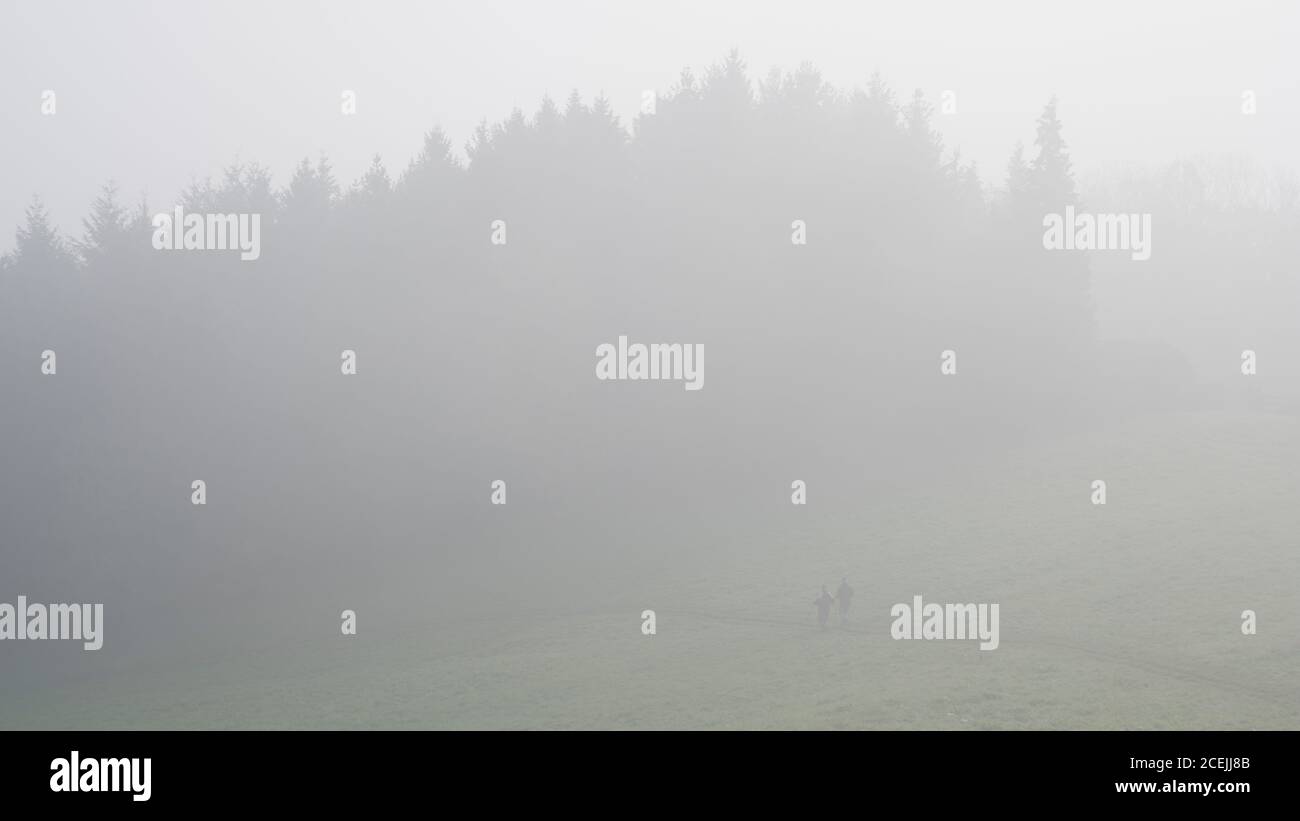 anonymous people walking in foggy meadow Stock Photo
