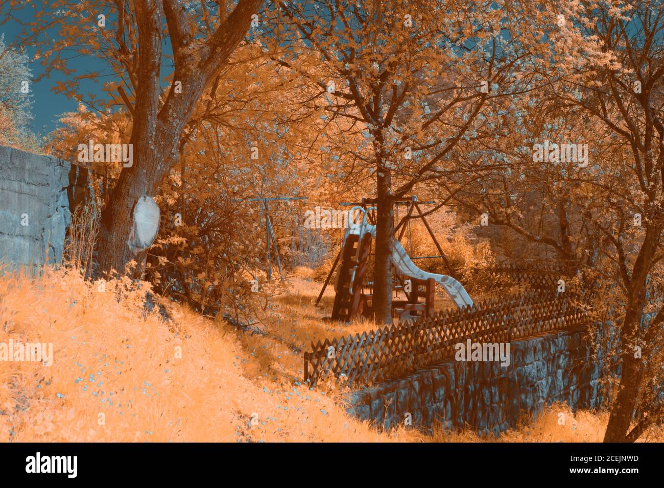 Infrared shot of tiny playground located amidst trees near fence in amazing countryside Stock Photo