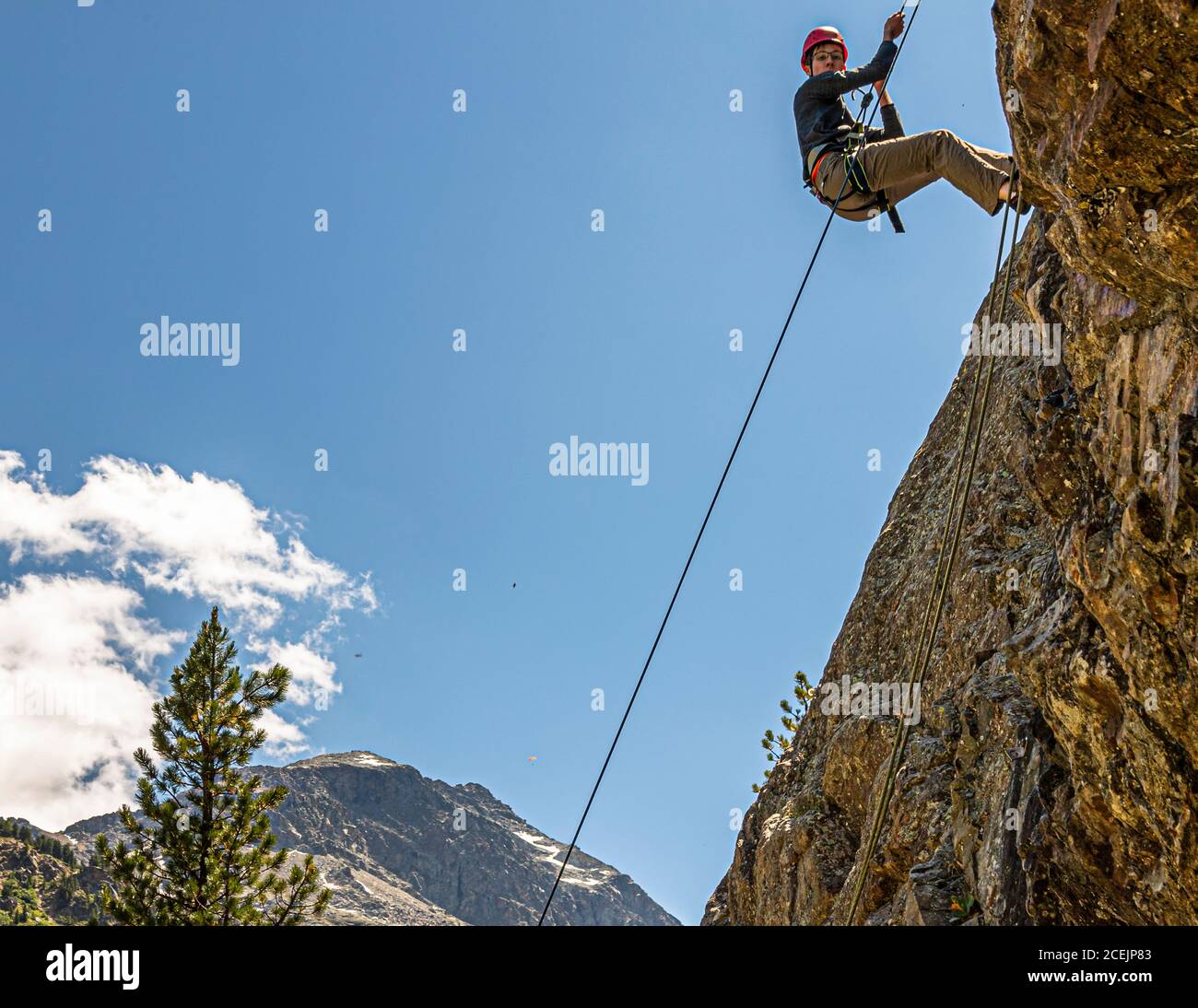 Young man roping down a rock in front of Piz Palü. Abseiling in front of the massif of Piz Palü is the reward at the end of the introductory climbing course. Rockclimbing in Pontresina, Switzerland Stock Photo