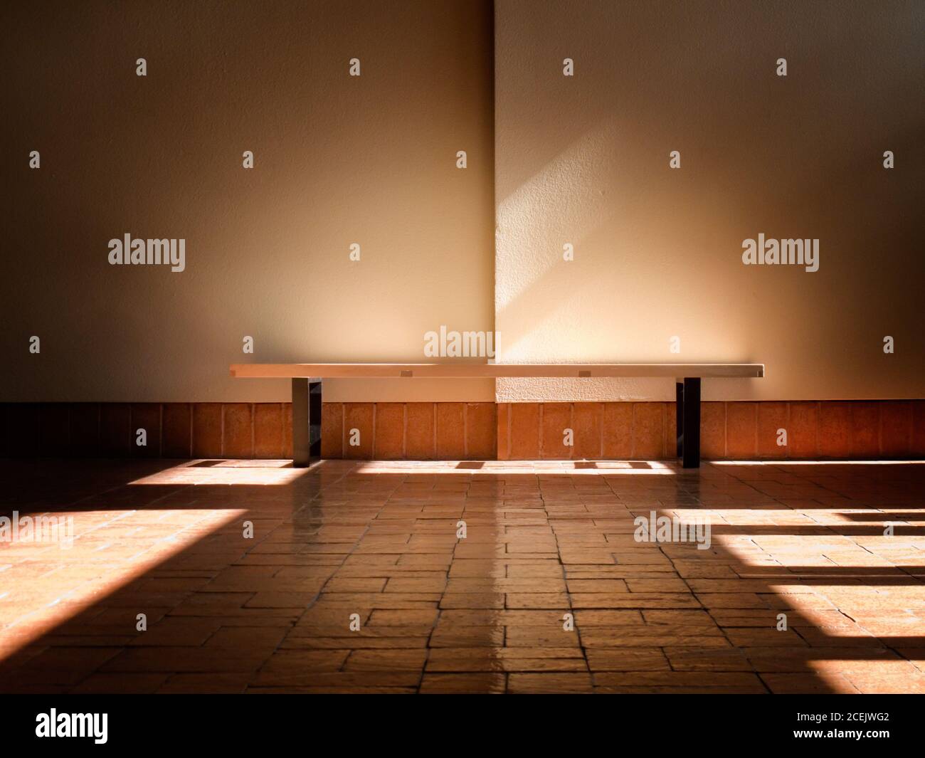 Interior shot of bench on stone floor in sunbeam against plain white wall Stock Photo