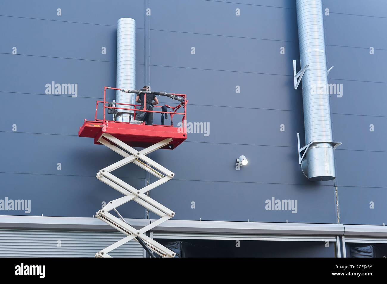 worker installs a ventilation system on the facade of a building using a  scissor lift Stock Photo - Alamy