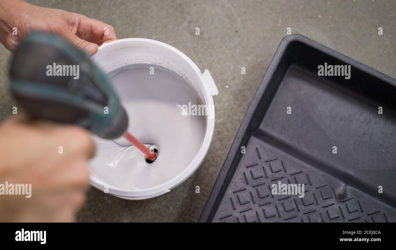 The white paint is mixed in a bucket with a drill. Drill paddle mixer