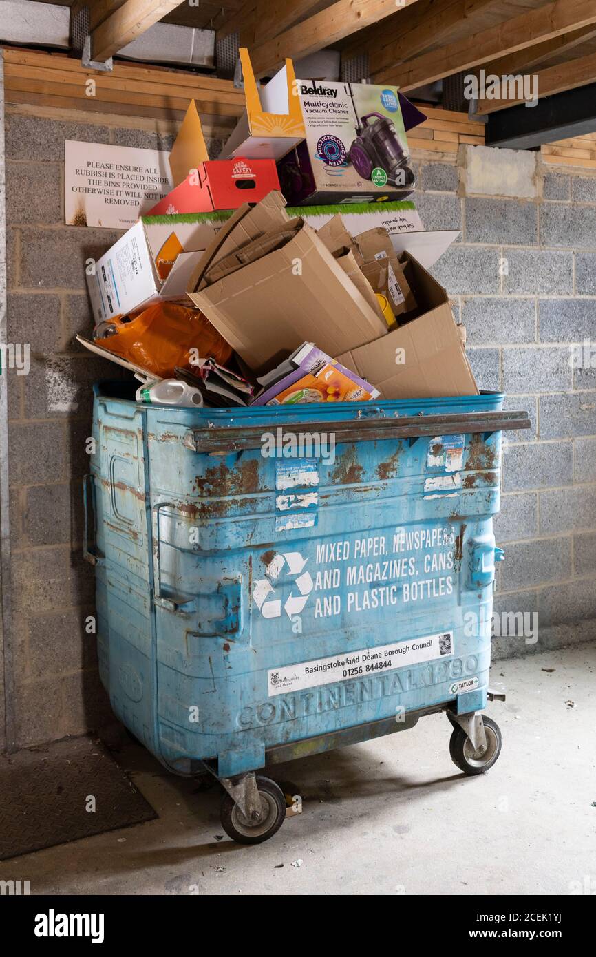 Cardboard boxes and other household recycling waste stacked high in a waste recycling bin for communal flats at Winterthur Way, Basingstoke, UK Stock Photo