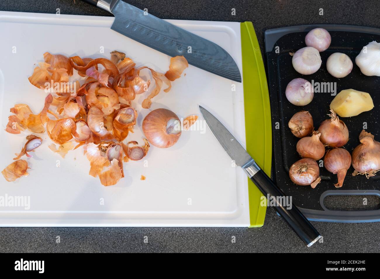 Peeled shallot onions with discarded onion skins on a white plastic chopping board with Japanese knives Stock Photo