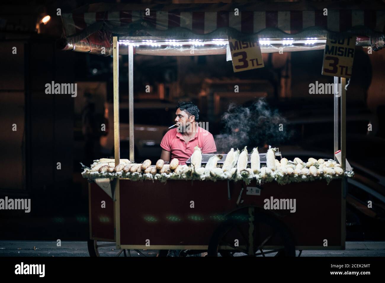 Istanbul, Turkey - July, 11 2018: Adult man sitting and smoking at counter with fresh corn at night Stock Photo