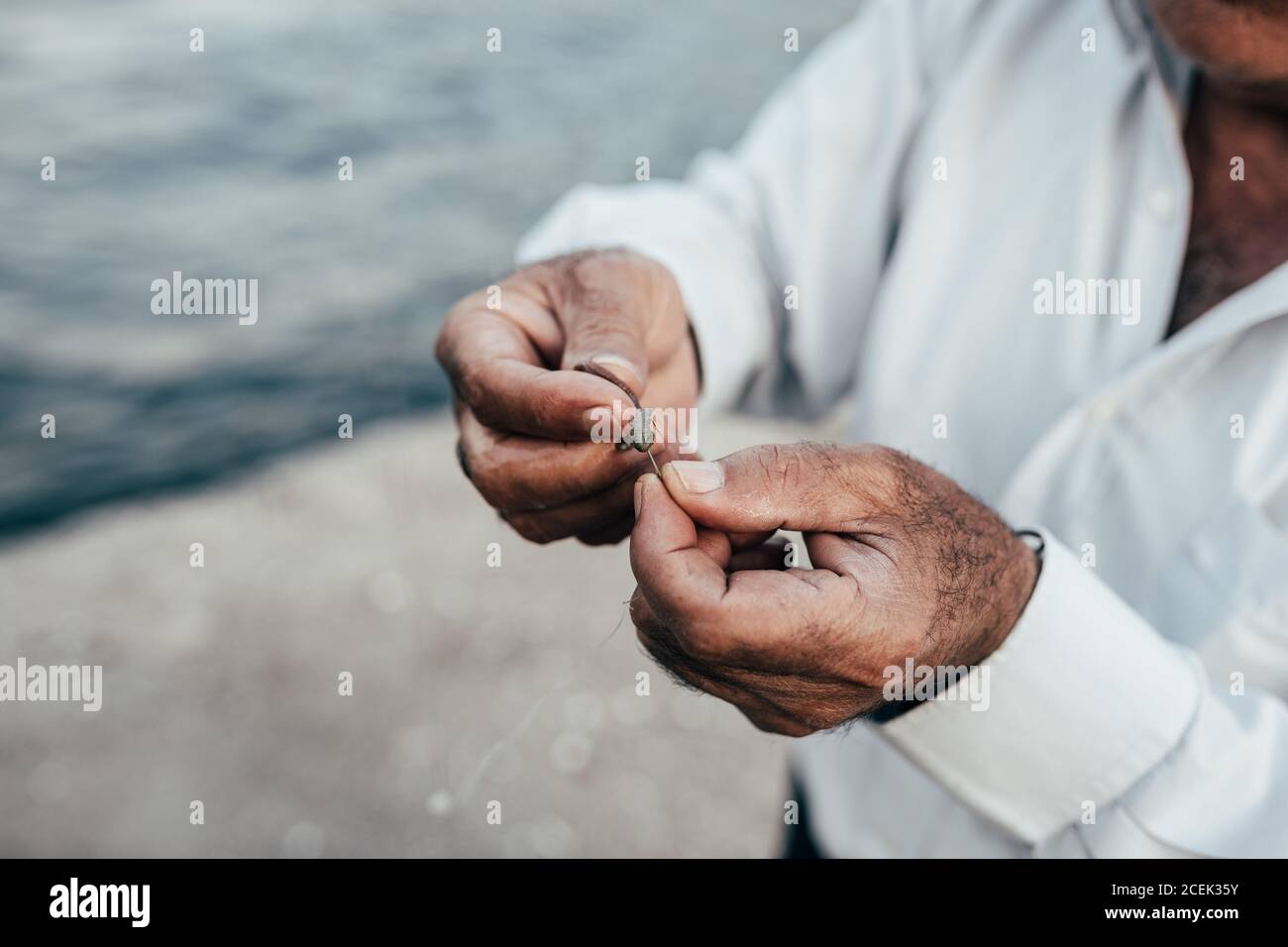 Crop hands of unrecognizable ethnic man holding plummet and preparing for fishing at water Stock Photo