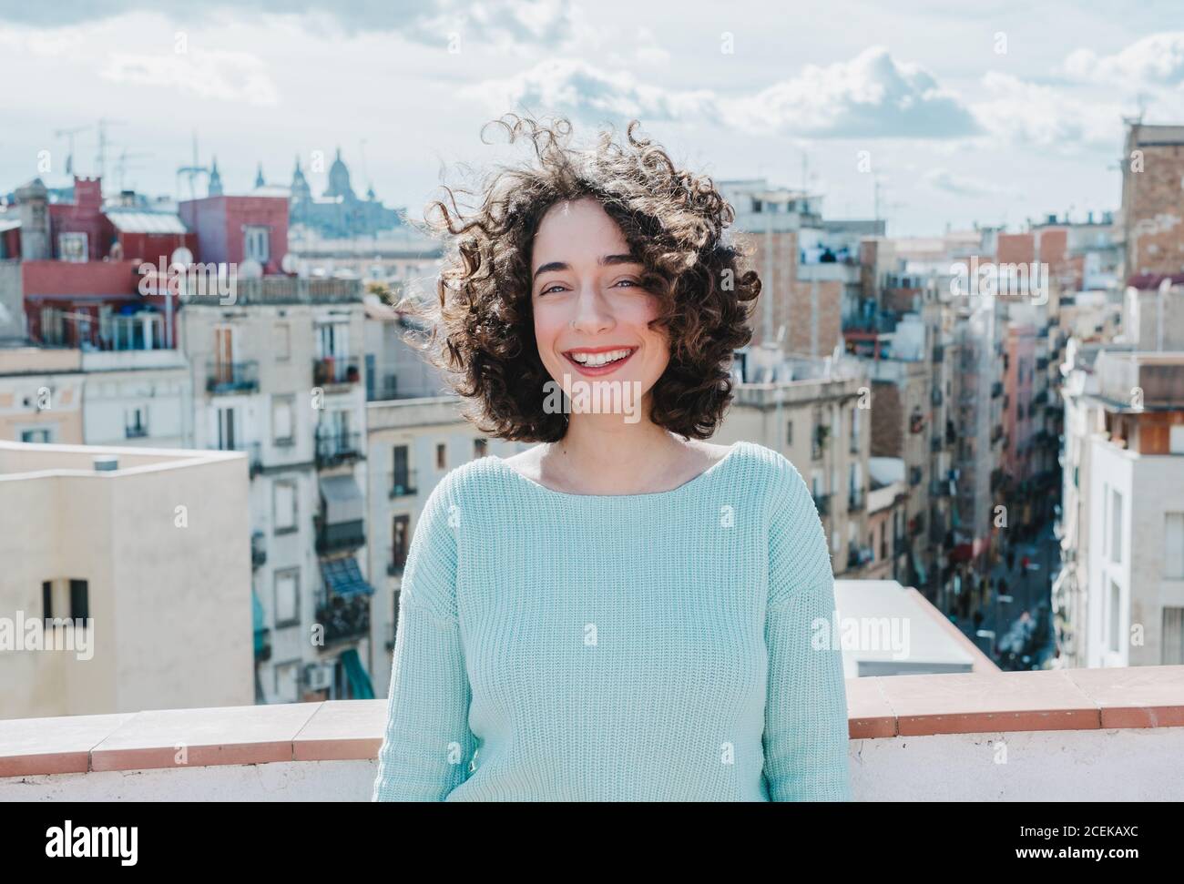 Pretty young brunette with curly hair smiling white standing on background of beautiful city. Stock Photo