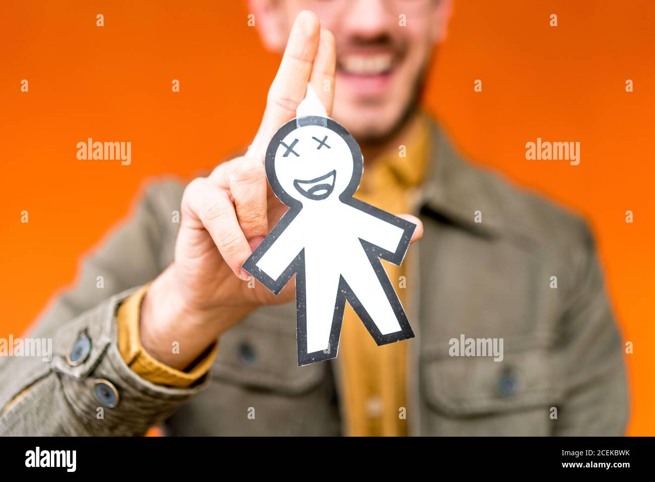 Happy guy showing paper silhouette for April fools day on orange blurred background Stock Photo