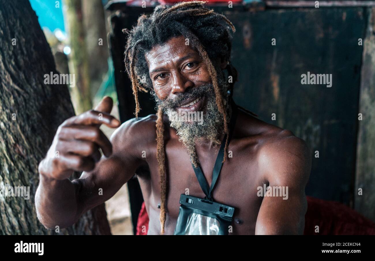 African American bearded male with dreadlocks and upped hands smoking cigar near trees Stock Photo