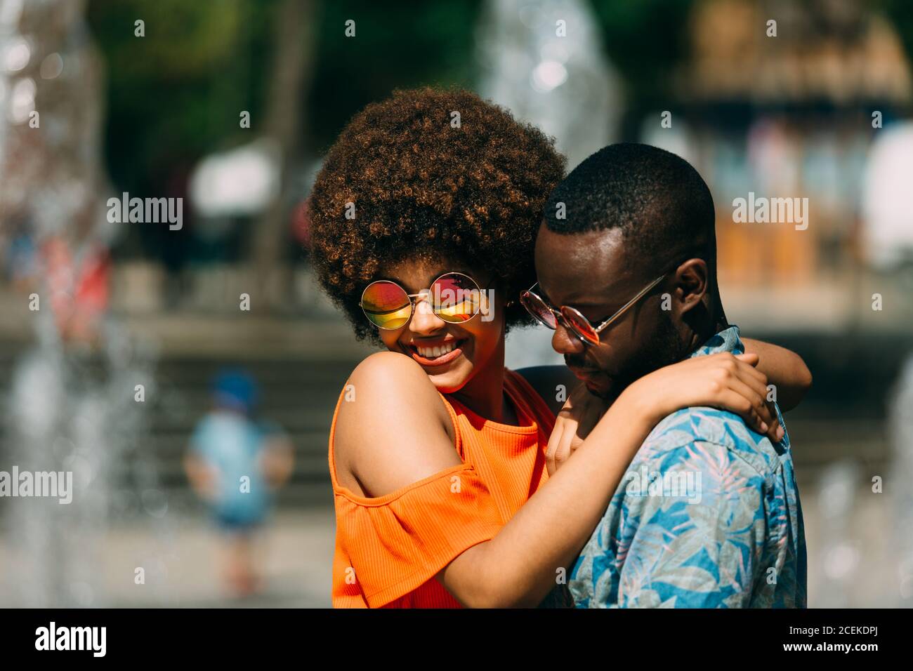 Handsome African-American man hugging pretty Woman and laughing while standing near fountain together Stock Photo