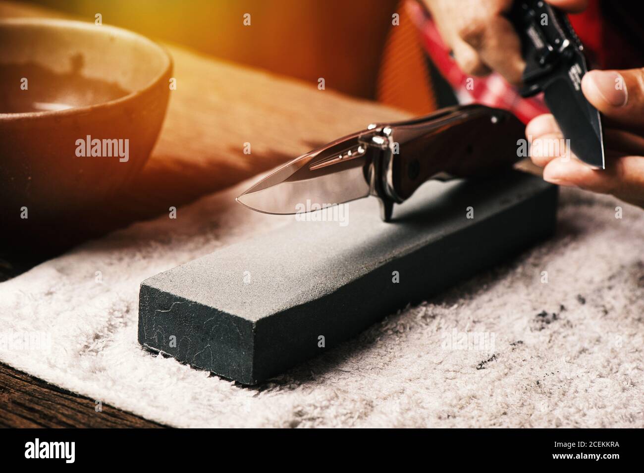 The man using whetstone to sharpening his pocket knife. Pocket knife