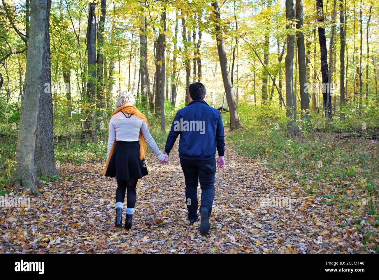 A young couple walking down a trail in the woods holding hands in the ...