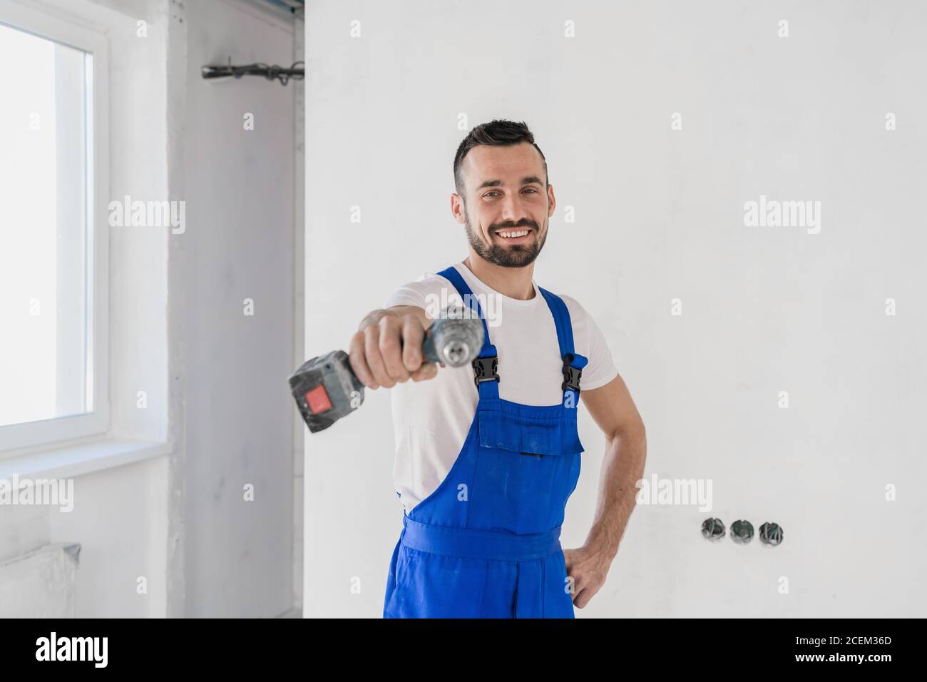 A young foreman holds a drill in his hand. He smiles and looks at the camera Stock Photo