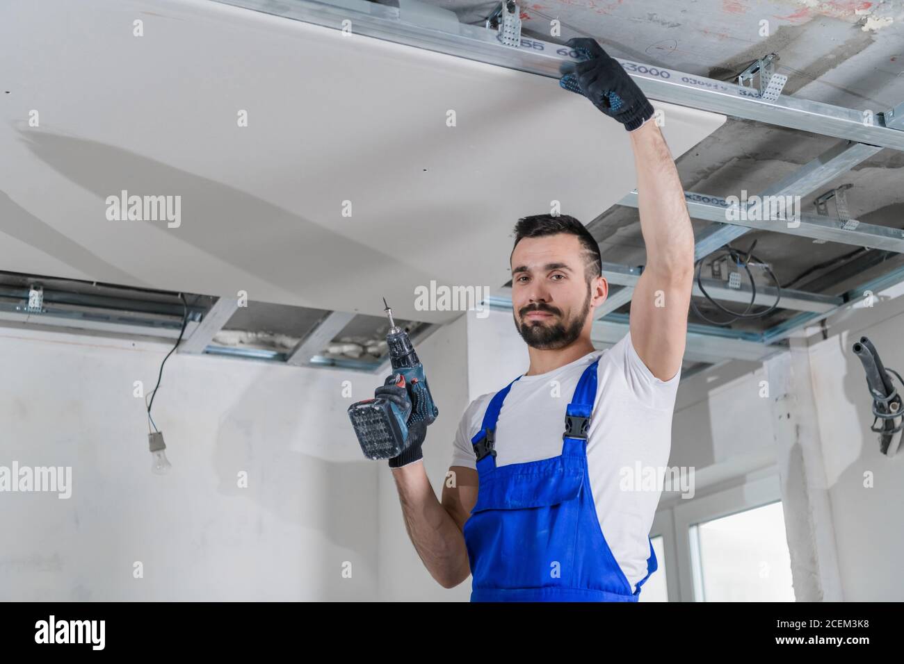 Fitter in blue overalls stand on a ladder and make a ceiling Stock Photo