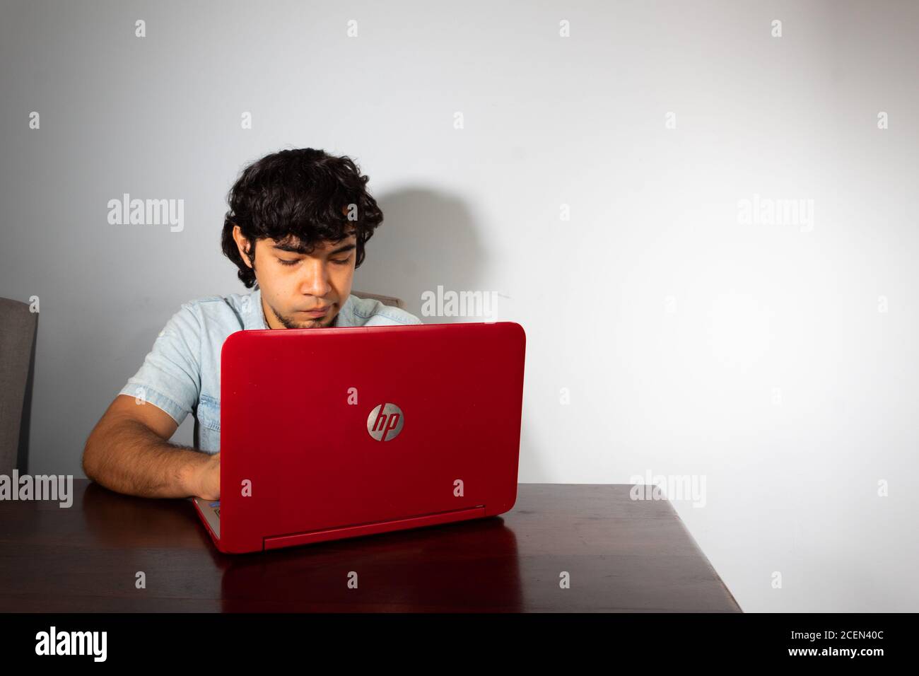 Young hispanic wavy hair man studying from home with a laptop, looking pensive Stock Photo