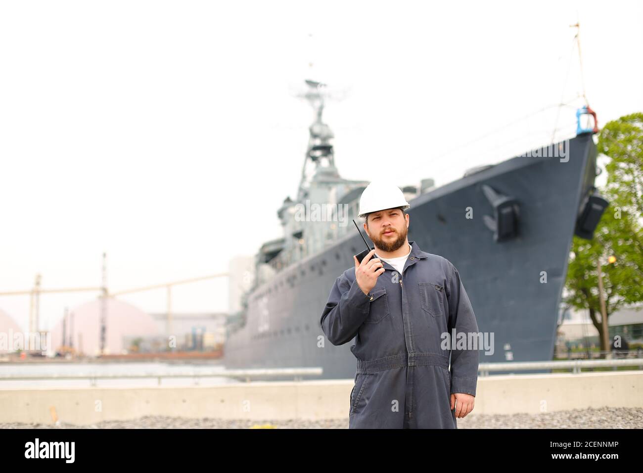 Marine deck officer talking by walkie talkie radio and standing near offshore vessel in bakground. Stock Photo
