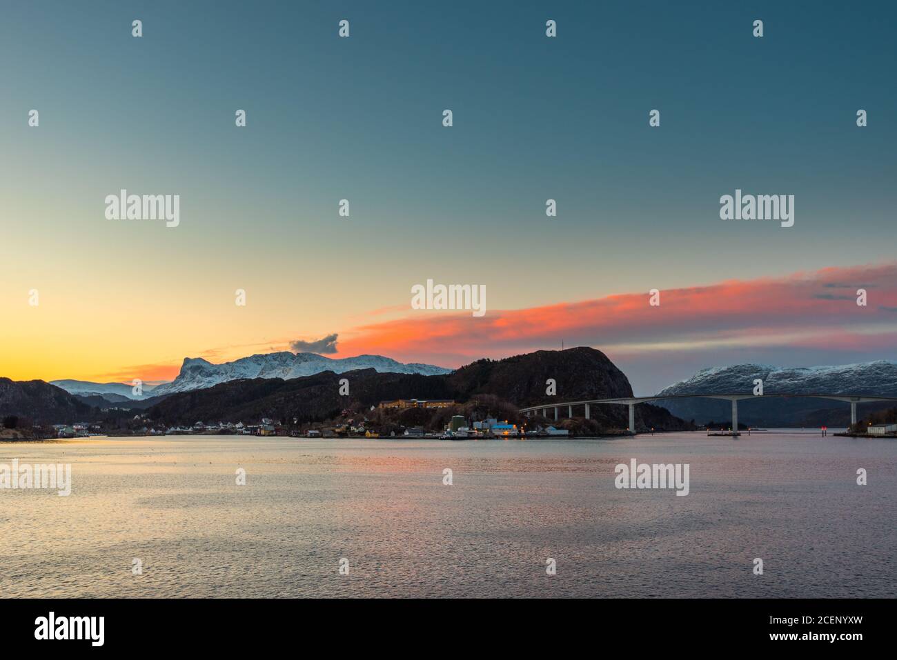 Colorful dawn over the coastline of Norway near the town Maloy with bridge, hills and snow capped mountains seen from cruise ship Stock Photo