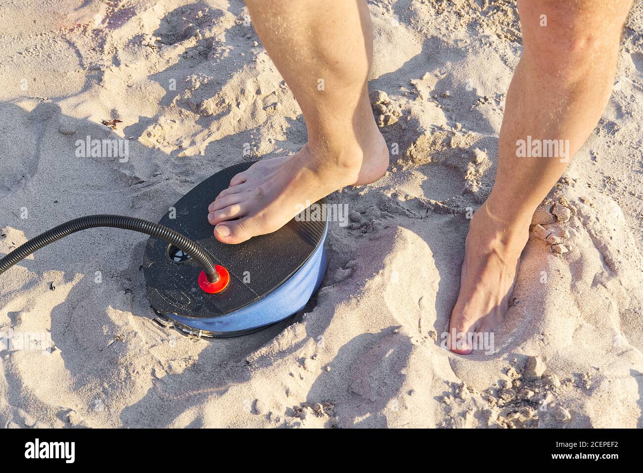 A Man with air foot pump pumps an inflatable mattress or air bed at sandy  beach. Foot inflates air mattress with foot pump on sand Stock Photo - Alamy