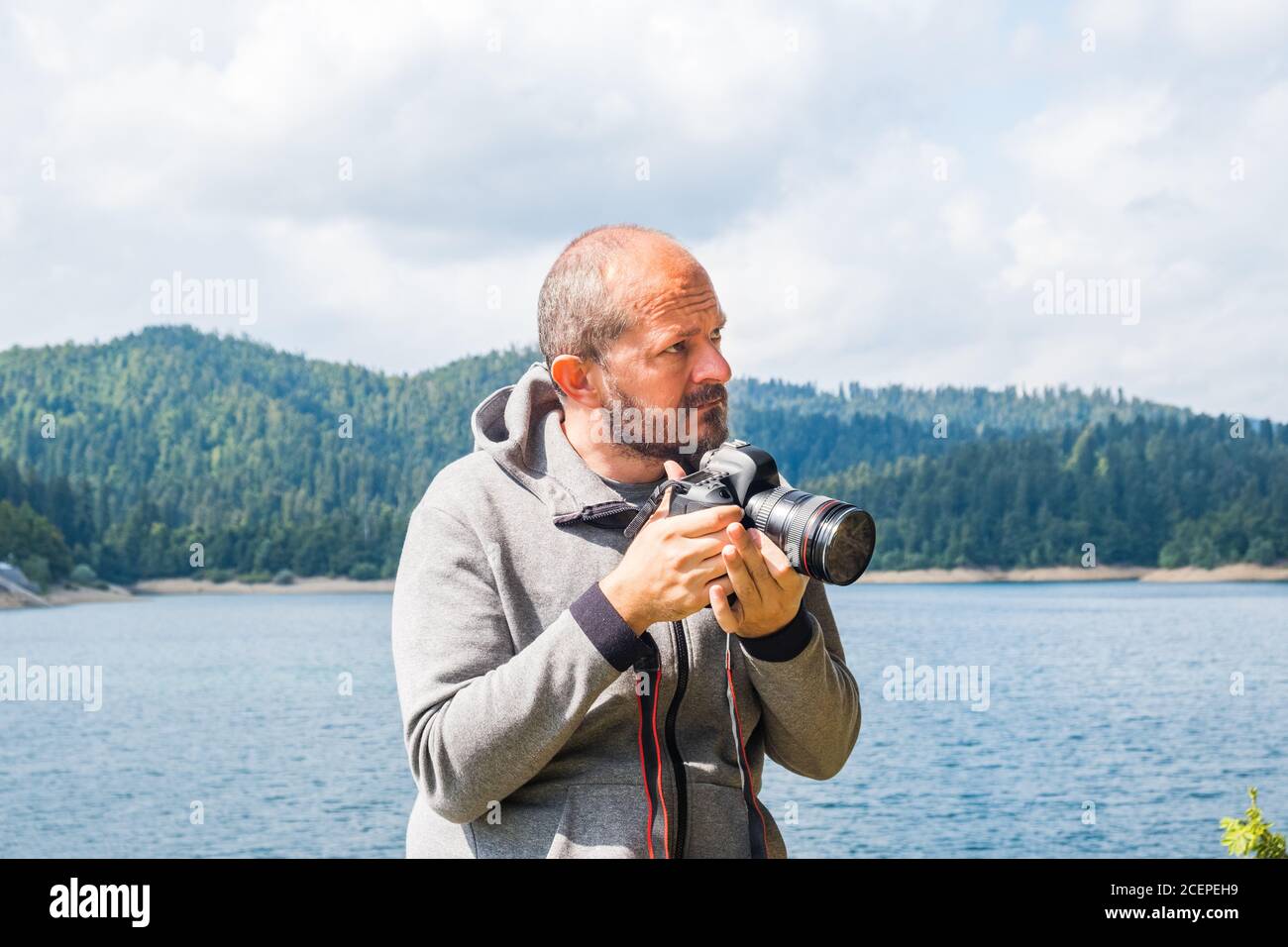 Photographer man in hoodie walking around lake with DSLR camera and shooting nature, half body portrait, landscape photography concept Stock Photo