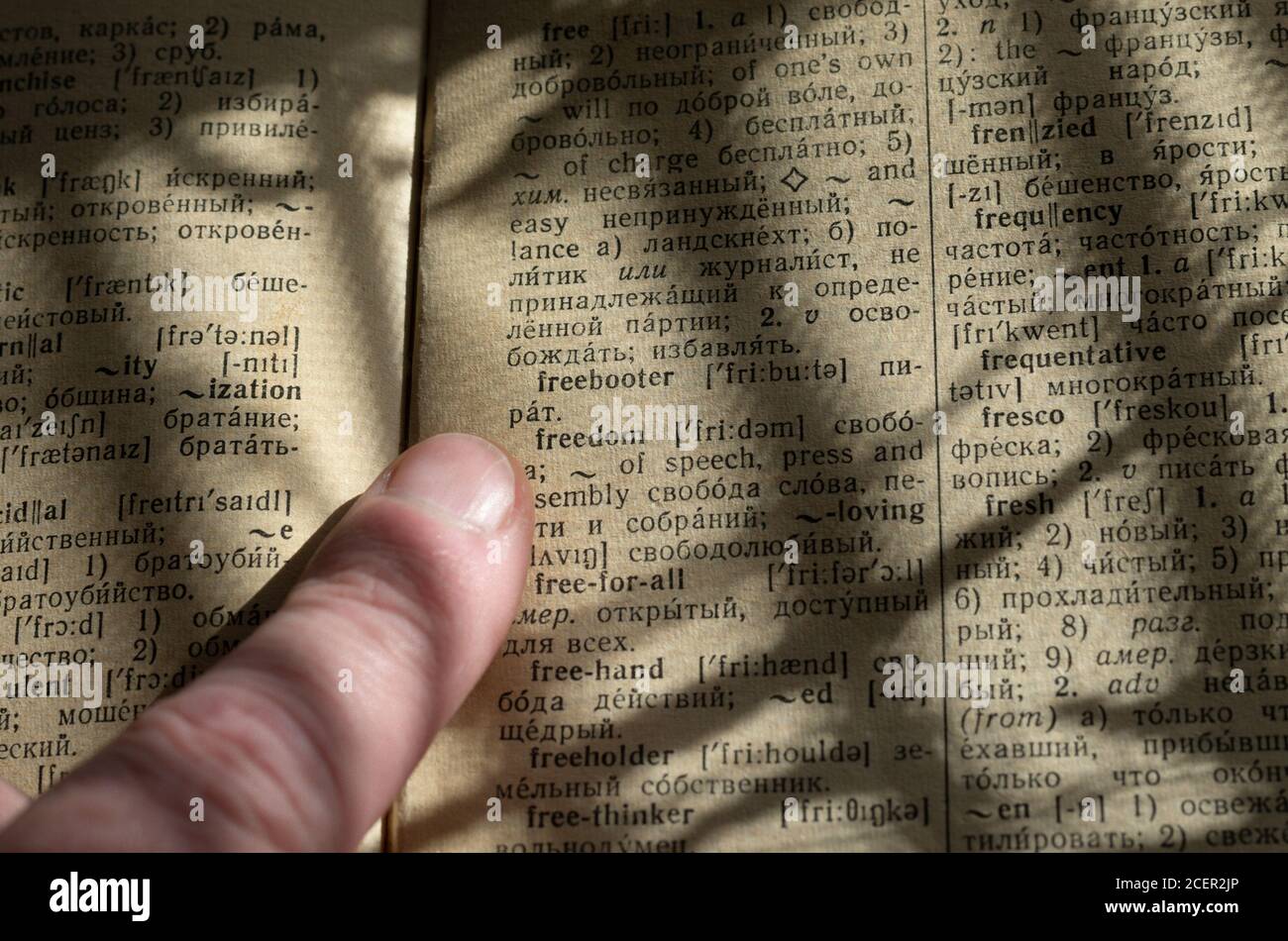 Forefinger is pointed at the word' freedom ' in a vintage dictionary with natural light and similar shadows in the form of prison bars Stock Photo