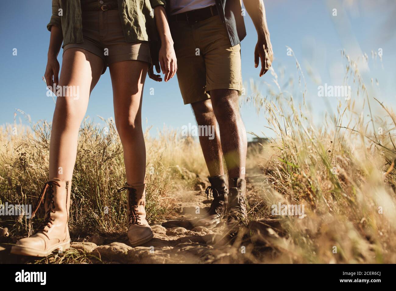 Close up of legs of two persons walking on a hiking trail. Couple walking on a rugged path wearing hiking shoes. Stock Photo